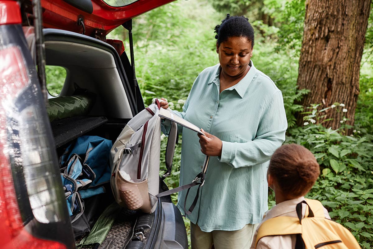 Adult getting a backpack out of the back of an SUV while looking at a kid wearing a backpack